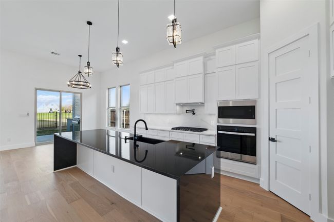 Kitchen featuring light wood-style flooring, a sink, dark countertops, and appliances with stainless steel finishes | Image 10