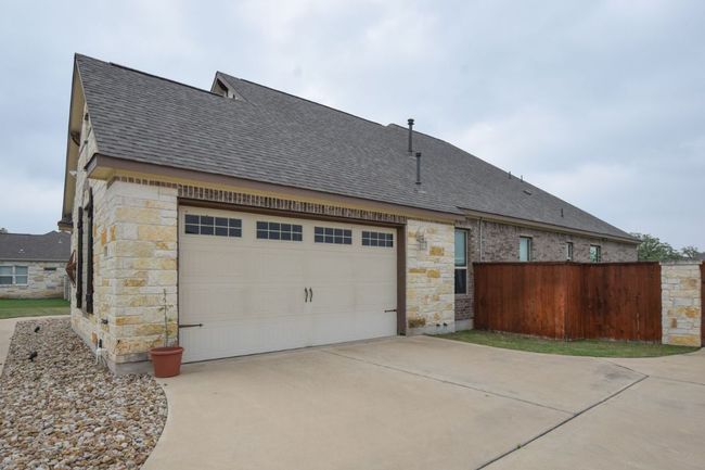View of property exterior with driveway, stone siding, roof with shingles, fence, and an attached garage | Image 24
