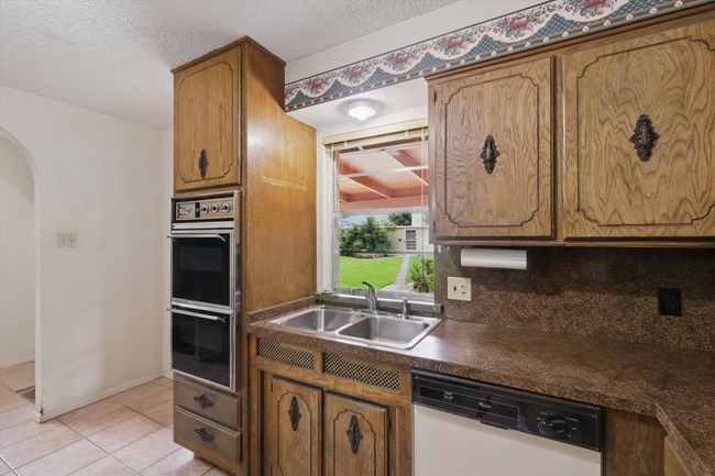 Kitchen with white dishwasher, double wall oven, a sink, arched walkways, and dark countertops | Image 21