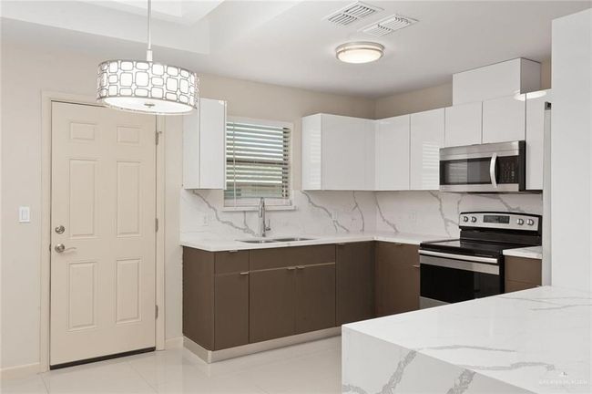 Kitchen with stainless steel appliances, decorative backsplash, white cabinets, and light stone countertops | Image 5
