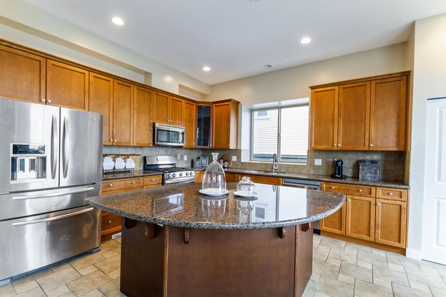 Kitchen with a center island, brown cabinets, a sink, dark stone countertops, and stainless steel appliances | Image 9