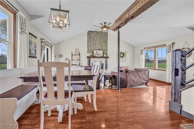 Dining room featuring baseboards, vaulted ceiling with beams, ceiling fan with notable chandelier, and wood finished floors | Image 10