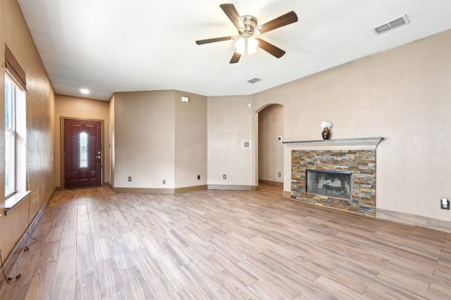 Unfurnished living room with arched walkways, ceiling fan, light wood-type flooring, a stone fireplace, and baseboards | Image 4