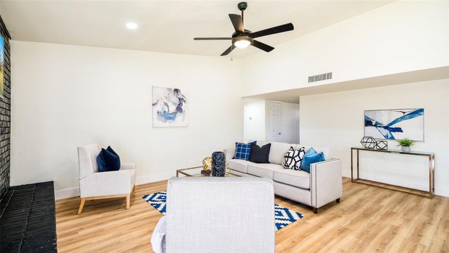 Living area featuring baseboards, light wood-type flooring, vaulted ceiling, a ceiling fan, and visible vents | Image 8