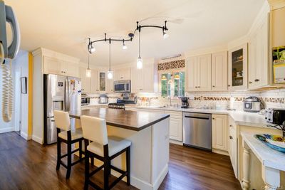 Kitchen with stainless steel appliances, wooden counters, a center island, sink, and dark wood-type flooring | Image 3