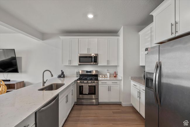 Kitchen with appliances with stainless steel finishes, white cabinets, light stone countertops, dark wood-style flooring, and recessed lighting | Image 9