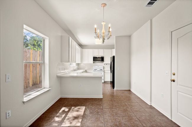 Kitchen featuring a chandelier, electric range, white cabinetry, light countertops, and a peninsula | Image 5