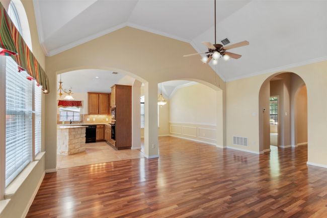 Unfurnished living room featuring plenty of natural light, ceiling fan, light wood-type flooring, high vaulted ceiling, and crown molding | Image 21