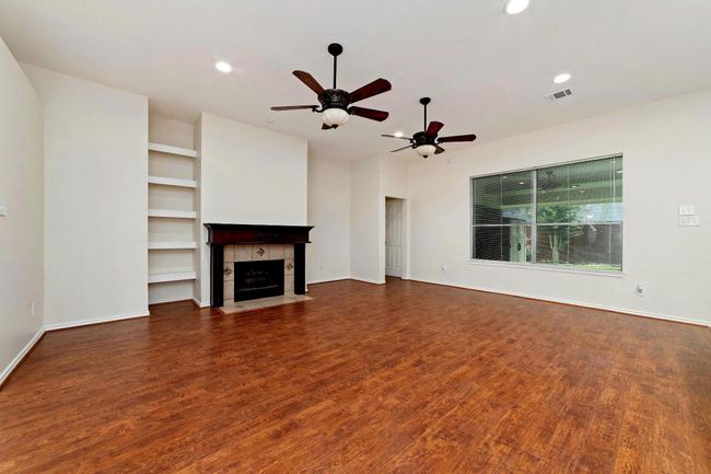 As the warmth of the floors flows beneath you, your space is beautifully accented by a striking cherry wood mantel framed with elegant tile surround. Soft canister lighting highlights the mantel’s details, creating a cozy and inviting atmosphere. Timeless ceiling fans blend classic design with modern functionality, perfectly complementing the room’s sophisticated style. | Image 7