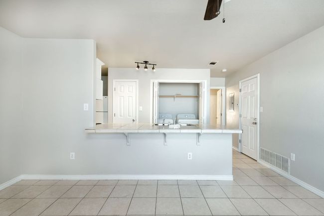Kitchen featuring tile countertops, separate washer and dryer, a kitchen bar, light tile patterned floors, and freestanding refrigerator | Image 6