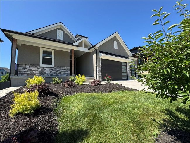 View of front of house with stucco siding, stone siding, a garage, driveway, and a front lawn | Image 69
