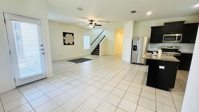 Kitchen with dark cabinetry, light tile patterned floors, decorative backsplash, stainless steel appliances, and a center island | Image 13