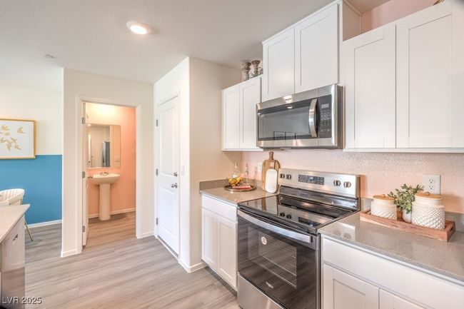 Kitchen featuring light stone counters, white cabinetry, appliances with stainless steel finishes, baseboards, and light wood-type flooring | Image 17