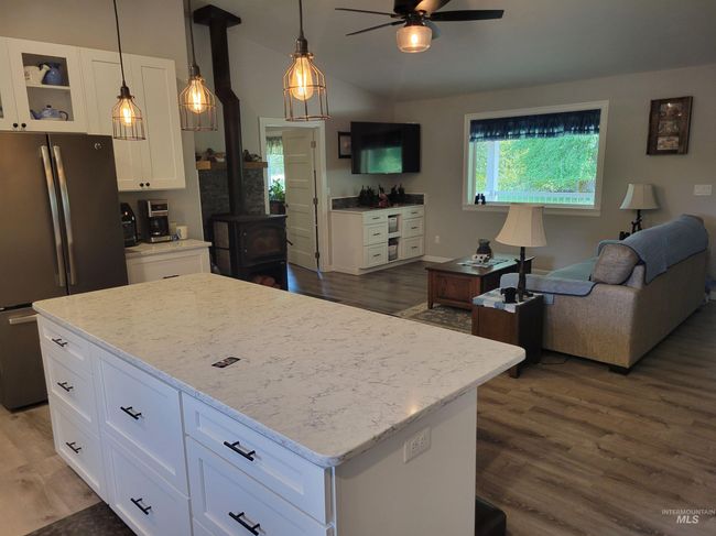 Kitchen featuring freestanding refrigerator, a wood stove, a ceiling fan, white cabinets, and wood finished floors | Image 15