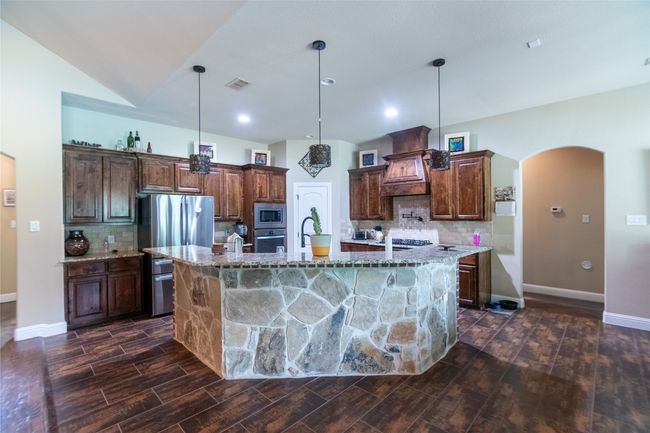 Kitchen featuring stainless steel appliances, arched walkways, a large island with sink, dark wood-type flooring, and tasteful backsplash | Image 14