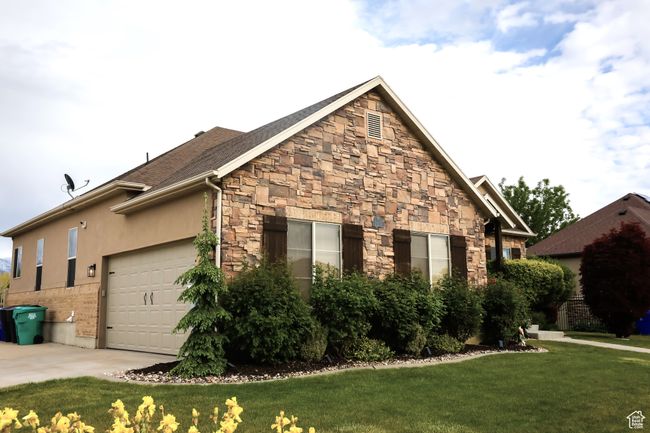 View of property exterior featuring a lawn, stone siding, a garage, and concrete driveway | Image 61