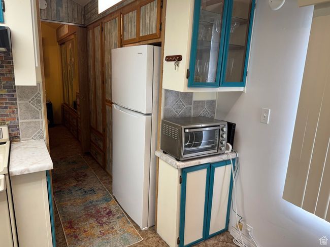 Kitchen featuring freestanding refrigerator, backsplash, light countertops, and glass insert cabinets | Image 8