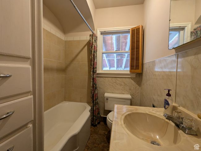 Bathroom with tile walls, shower / bath combo with shower curtain, toilet, wainscoting, and vanity | Image 11