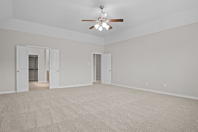 Unfurnished bedroom with light colored carpet, a ceiling fan, baseboards, and a walk in closet | Image 20