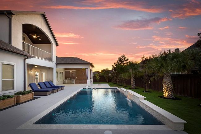 This backyard oasis features a stunning heated pool, sleek water features, and a glowing landscape that comes alive at sunset. With a covered balcony above and a fully equipped outdoor kitchen nearby, this space is designed for year-round relaxation and entertaining. | Image 39