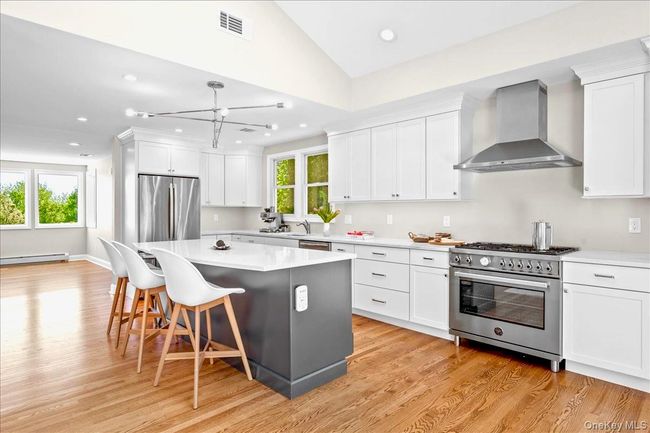 Kitchen featuring wall chimney range hood, stainless steel appliances, light wood-style floors, a breakfast bar area, and a baseboard | Image 12