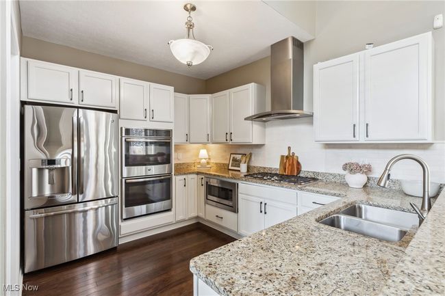 Kitchen featuring white cabinetry, stainless steel appliances, double ovens, granite countertops, stainless vent hood, and built-in microwave | Image 13
