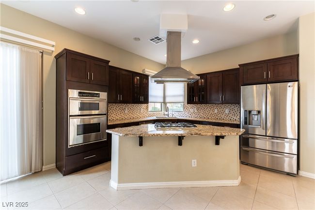 Kitchen featuring decorative backsplash, a breakfast bar, appliances with stainless steel finishes, light stone counters, and a center island | Image 8