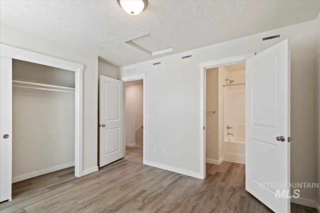 Unfurnished bedroom featuring a textured ceiling, attic access, light wood-style floors, and a closet | Image 10