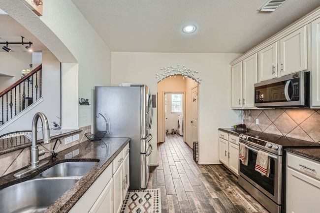 Kitchen with stainless steel appliances, arched walkways, backsplash, dark wood-style flooring, and dark stone counters | Image 15