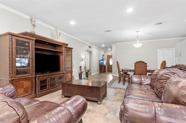 This is a spacious, well-lit living room with a large entertainment unit, leather sofas, and an open-plan layout leading to a dining area. The room features recessed lighting, neutral wall colors, and tile flooring, creating a comfortable and versatile space. | Image 18