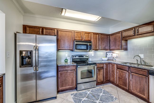 The kitchen boasts gorgeous granite countertops and a sleek subway tile backsplash, complimented by under cabinet lighting. Stainless steel appliances provide a modern aesthetic while a chic tile floor completes the picture. | Image 8