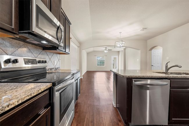 Kitchen with stainless steel appliances, arched walkways, decorative backsplash, dark wood-type flooring, and ceiling fan | Image 12