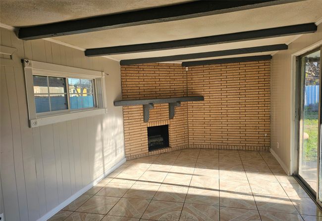 Unfurnished living room featuring beamed ceiling, a brick fireplace, healthy amount of natural light, wood walls, and brick wall | Image 12