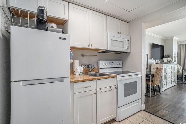 Kitchen with white appliances, ornamental molding, white cabinets, light countertops, and light tile patterned floors | Image 11