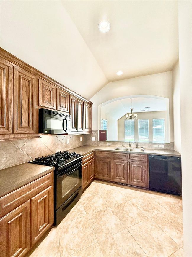 This kitchen features warm wood cabinetry, a gas stove, and a built-in microwave. It has a spacious layout with tiled flooring, a double sink, and a dishwasher, offering a bright and inviting atmosphere. | Image 6