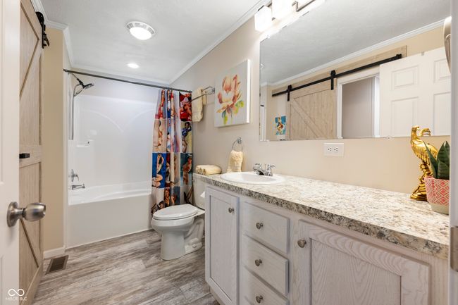 bathroom with crown molding, wood finished floors, vanity, toilet, and shower / bath combo with shower curtain | Image 24
