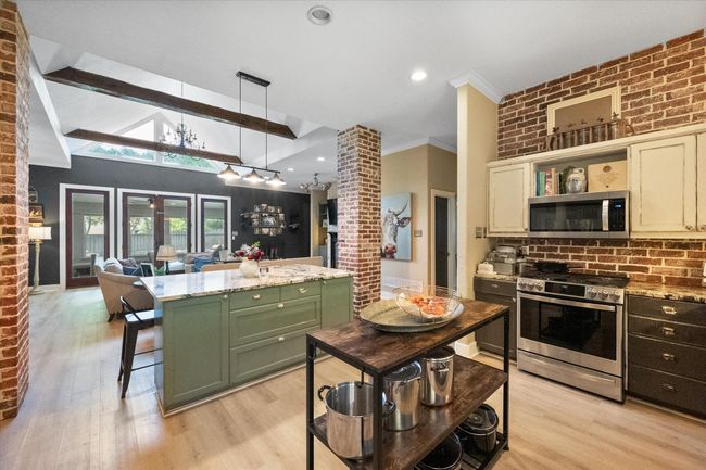 Kitchen with appliances with stainless steel finishes, green cabinetry, light wood-style floors, open shelves, and brick wall | Image 10