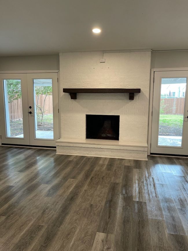 Unfurnished living room with french doors, a healthy amount of sunlight, dark wood-type flooring, and a brick fireplace | Image 13
