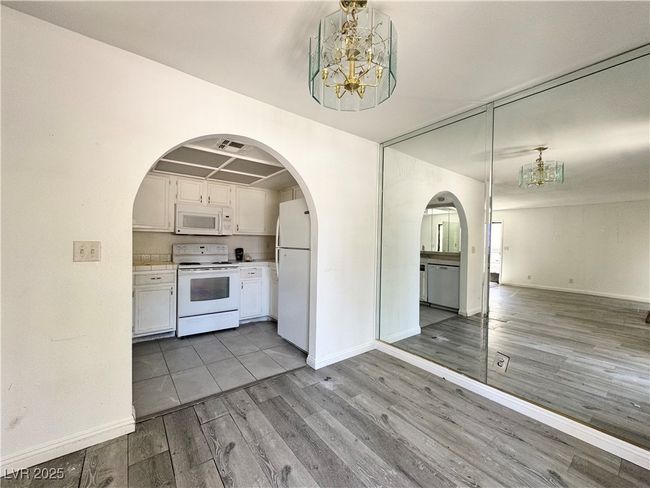 Kitchen with white appliances, a chandelier, wood finished floors, and open floor plan | Image 8