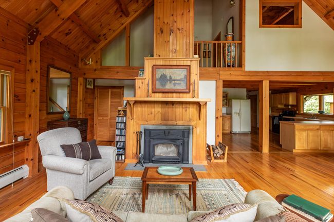 Living area featuring high vaulted ceiling, wooden walls, a baseboard radiator, light wood-type flooring, and wood ceiling with exposed beams | Image 8