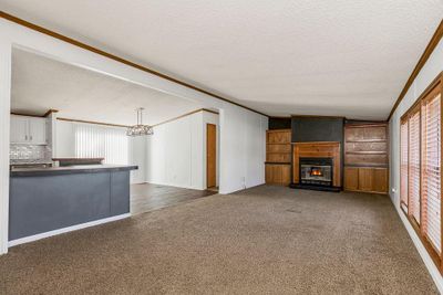 Carpeted living room which is open to kitchen/dining area, features a woodburning fireplace, built-in shelving/cabinets, a textured ceiling, and ornamental molding | Image 3