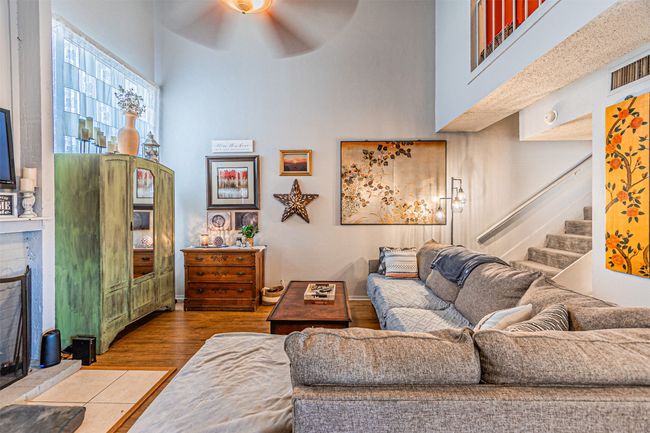 Living area with a high ceiling, ceiling fan, a fireplace with raised hearth, stairs, and wood finished floors | Image 5