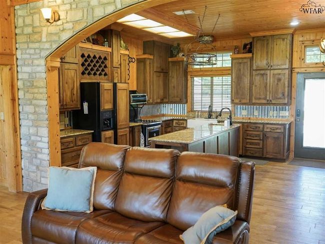 Kitchen with decorative backsplash, wooden ceiling, black fridge with ice dispenser, light hardwood / wood-style flooring, and stainless steel range oven | Image 4