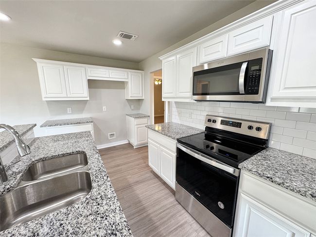 Kitchen featuring stainless steel appliances, light wood finished floors, white cabinets, recessed lighting, and backsplash | Image 4