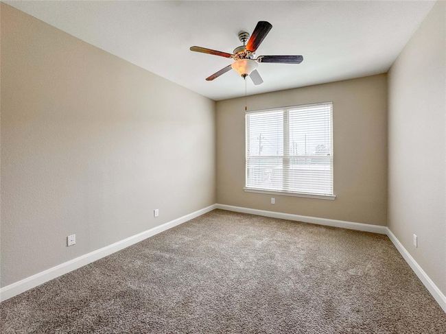 This secondary bedroom features neutral walls, a plush carpet, and a ceiling fan. It has a large window that allows natural light to fill the space, creating a bright and inviting atmosphere. | Image 15
