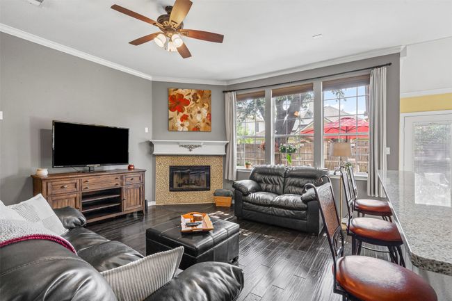 Living area featuring a ceiling fan, crown molding, dark wood-type flooring, and a glass covered fireplace | Image 4