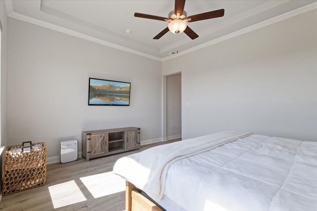 Bedroom with wood finished floors, baseboards, crown molding, a raised ceiling, and a ceiling fan | Image 21