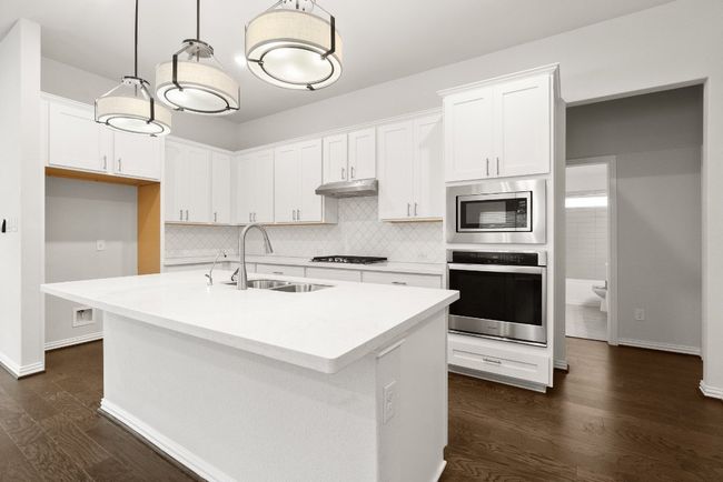 Kitchen with decorative backsplash, stainless steel appliances, white cabinetry, and an island with sink | Image 7