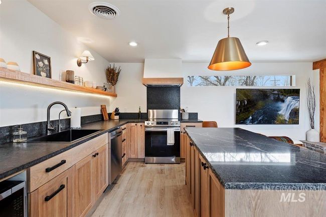 Kitchen featuring stainless steel appliances, premium range hood, open shelves, light wood-style flooring, and decorative light fixtures | Image 37
