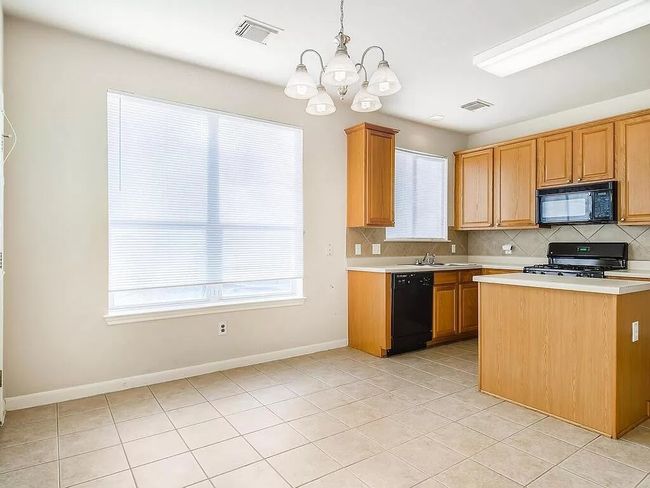 Kitchen with black appliances, a chandelier, light countertops, decorative backsplash, and light tile patterned flooring | Image 12